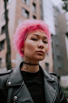 一位身穿皮夹克、纹着身的时尚粉发女子，在户外自信地摆着姿势
