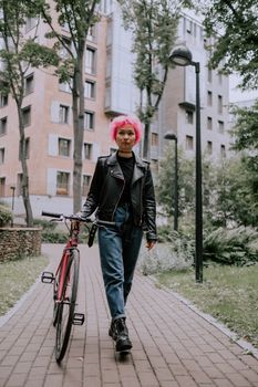 一位身穿黑色皮夹克的时尚女士骑着粉色自行车，沿着城市小路骑行，尽显都市时尚