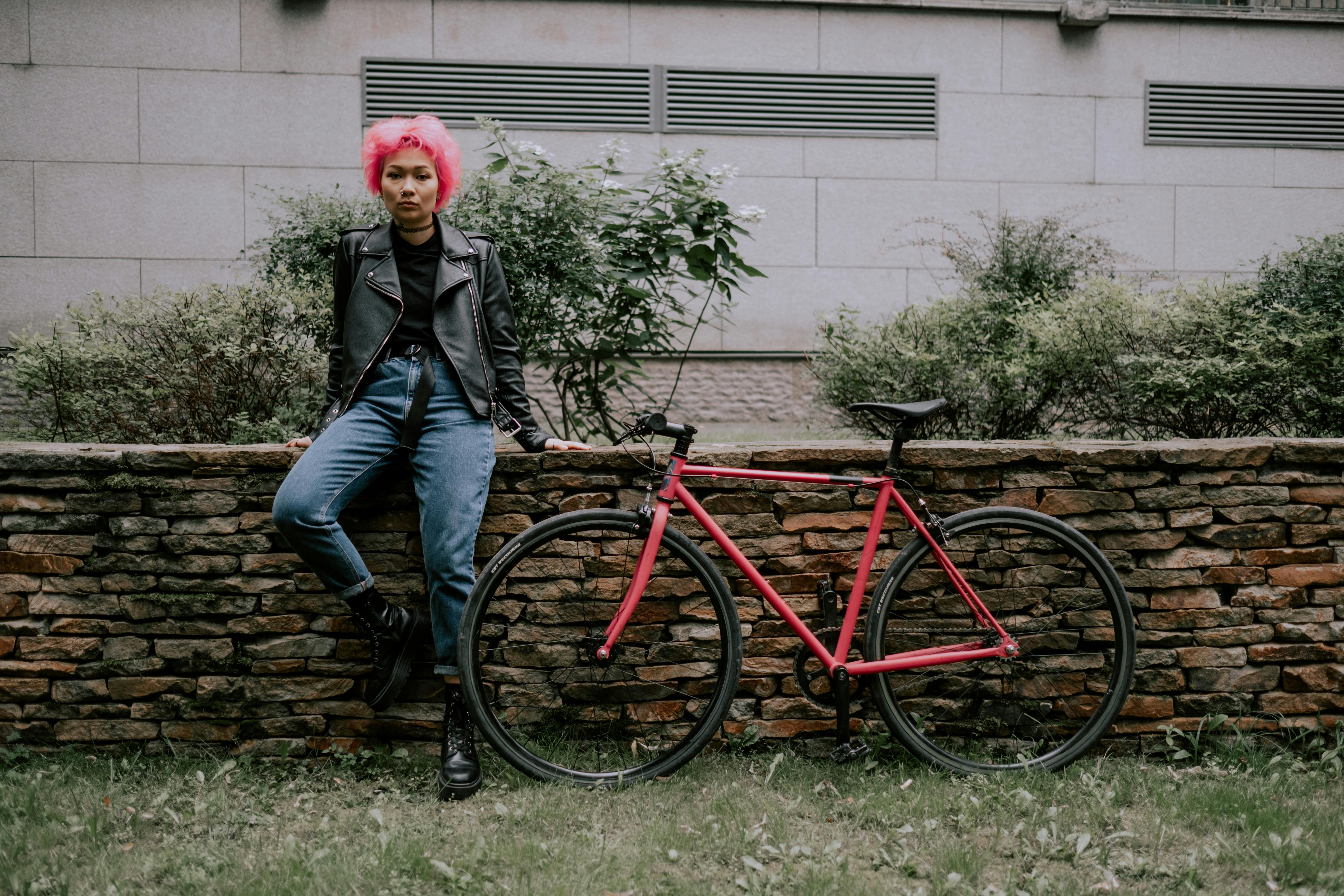 woman in black jacket and blue denim jeans standing beside red bicycle