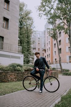 穿着牛仔布和毛衣的时尚年轻人，在住宅区户外骑着自行车摆姿势