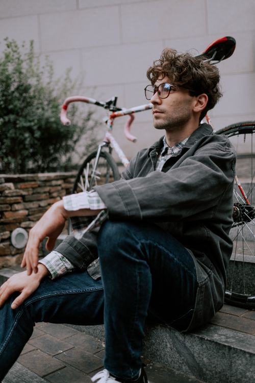 Free Stylish man in casual attire sitting by his bicycle in an urban setting. Stock Photo