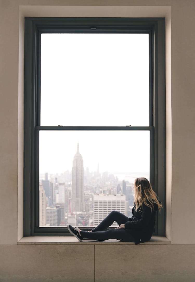 A Woman Sitting On Window Sill At The Top Of The Rock In New York City