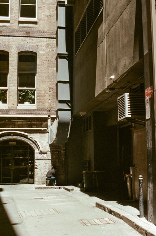 Free A sunlit urban alleyway with a sitting person near a historic brick facade. Stock Photo