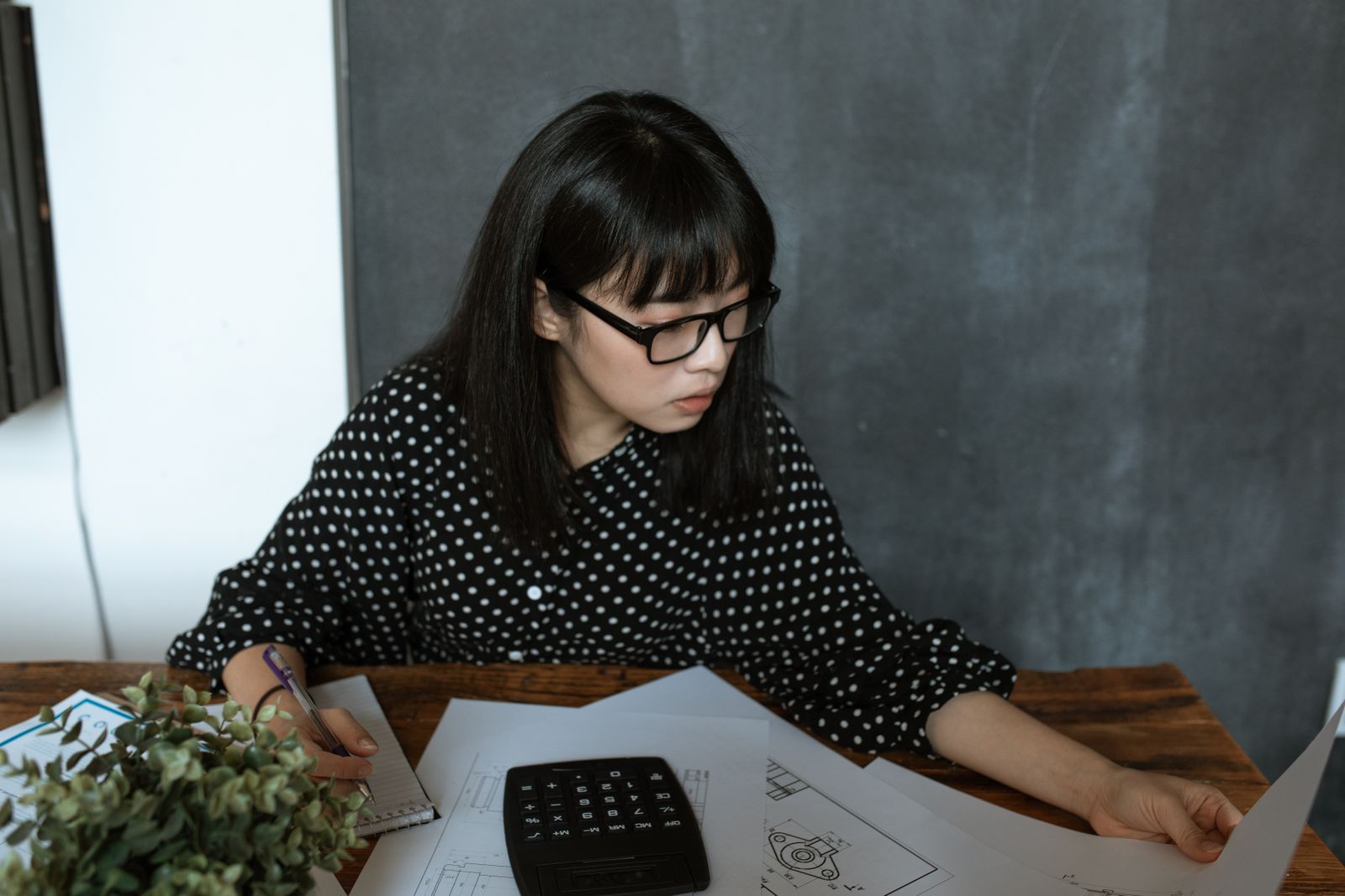 Asian woman na nagrereview ng financial paperwork gamit ang calculator
