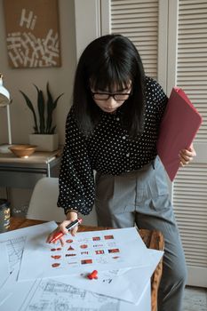一位亚洲女性正在家庭办公桌前审阅设计文件，重点关注创造力和创新