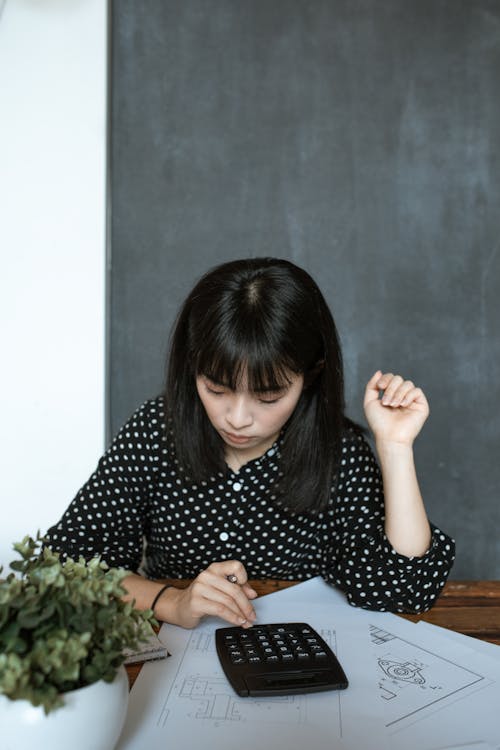 A Woman Wearing a Polka Dot Blouse Using a Calculator