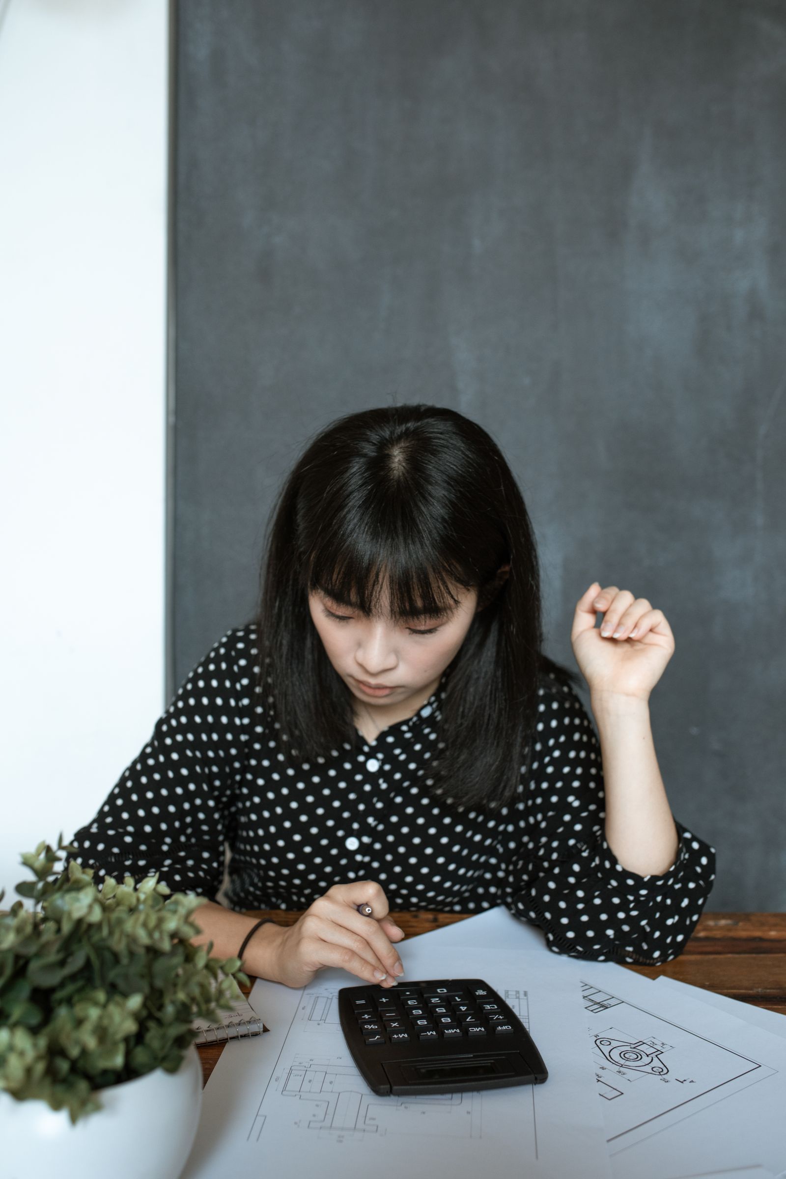 Asian woman na gumagamit ng calculator at financial documents para ihambing ang mga utang