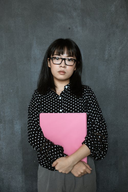 A Woman Holding a Pink Folder Standing in Front of a Gray Wall