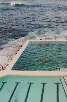 A swimmer in an oceanfront pool with waves crashing nearby, offering a scenic coastal experience.