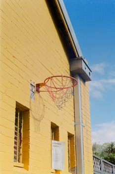 Low angle view of a basketball hoop on a yellow brick wall, under a clear blue sky.