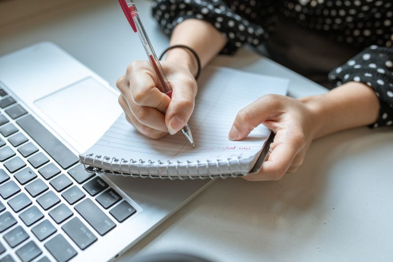 Person writing and planning alongside a laptop