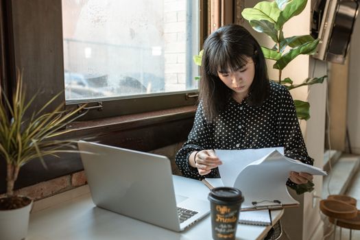 在自然光线充足的现代办公环境中，一位亚洲女商人正在审查文件