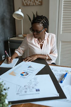 African businesswoman concentrating on planning with charts and diagrams in a modern workspace.