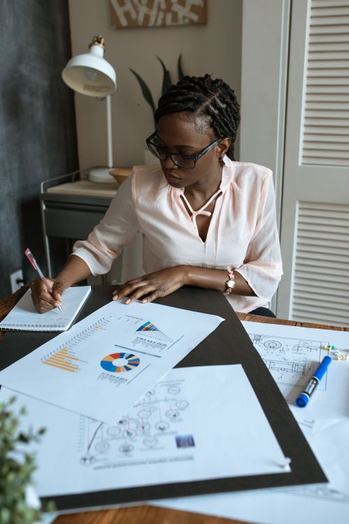 Free African businesswoman concentrating on planning with charts and diagrams in a modern workspace. Stock Photo