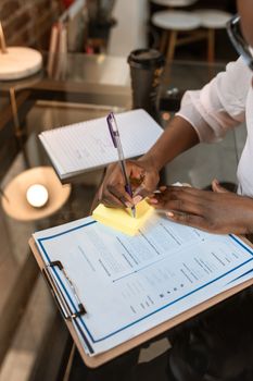 A businesswoman writes notes on a clipboard with documents in a modern office setting. 5915206