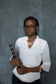 Black woman in eyeglasses holding a binder stands confidently against a gray textured wall.