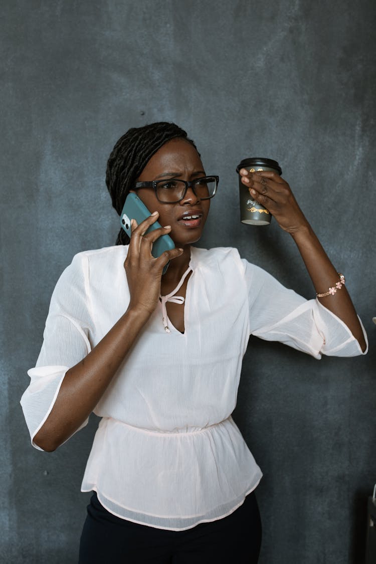 Annoyed Woman Talking On The Phone While Holding A Coffee Cup