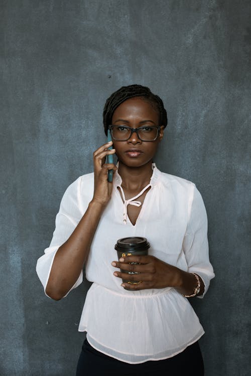 Woman Holding A Cup of Coffee While Using Cellphone