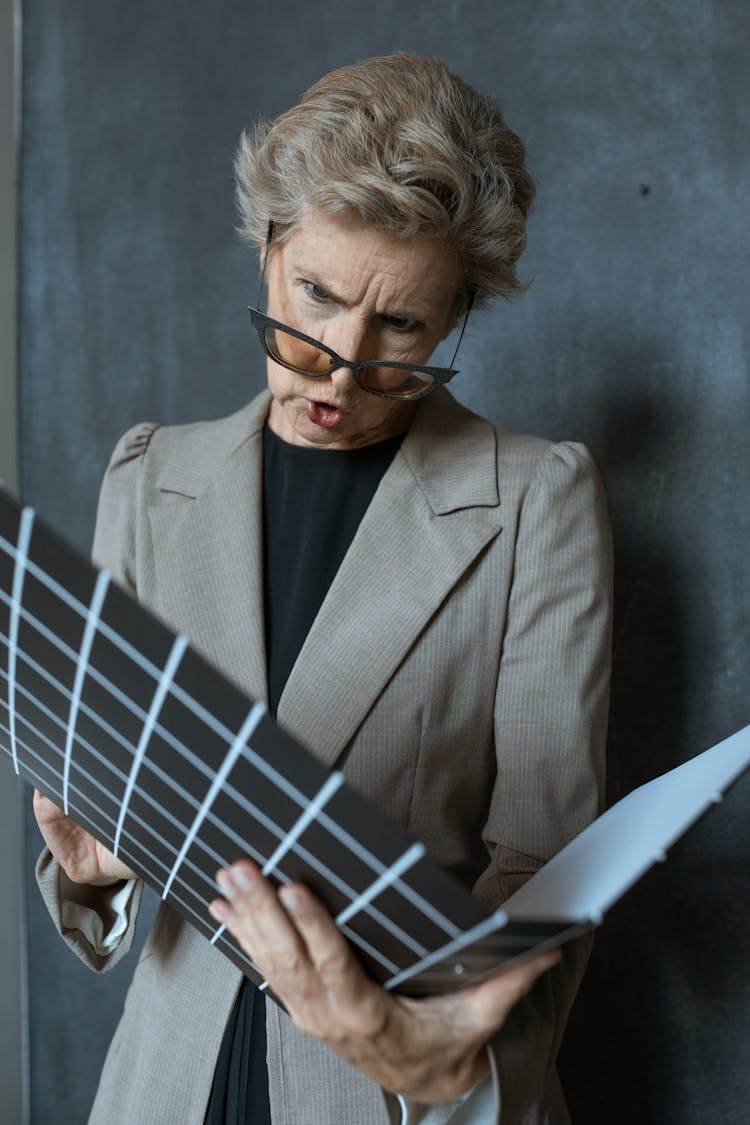 An Elderly Woman Reading A Document On A Binder