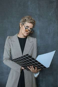 一位戴着眼镜、穿着灰色外套的老妇人正在研究灰色墙壁上的粘合剂