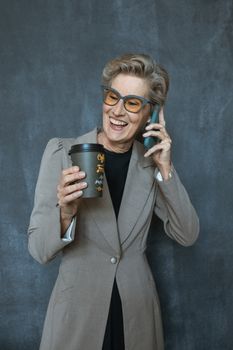 一位穿着外套、气质优雅的女士端着咖啡，微笑着用智能手机通话
