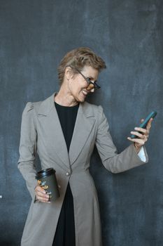 一位自信的资深女商人在现代办公室里对着她的智能手机微笑