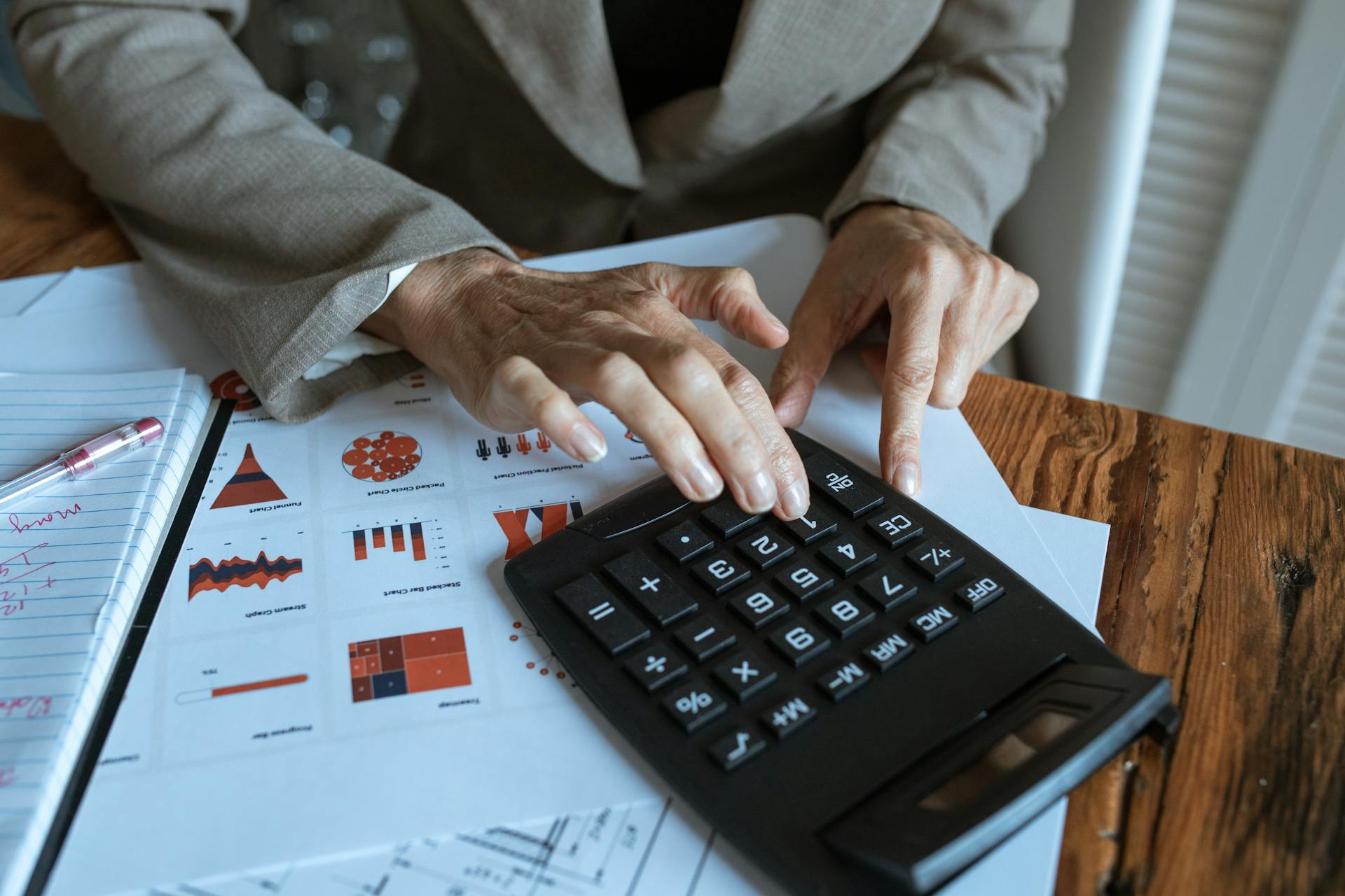 A businessman using a calculator to analyze financial charts and graphs on a desk.