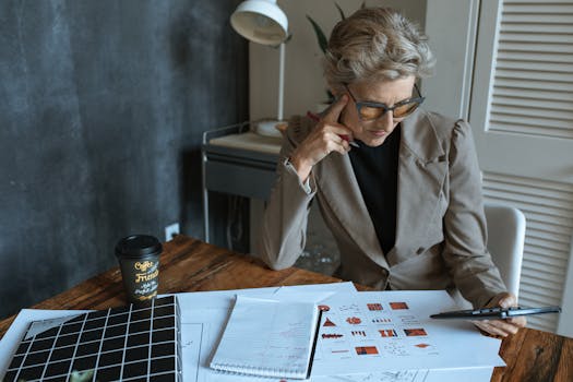 Focused businesswoman reviewing documents at desk in modern home office setting.