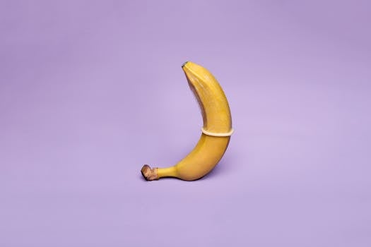 A banana wearing a condom symbolizes safe sex education against a pastel purple background.