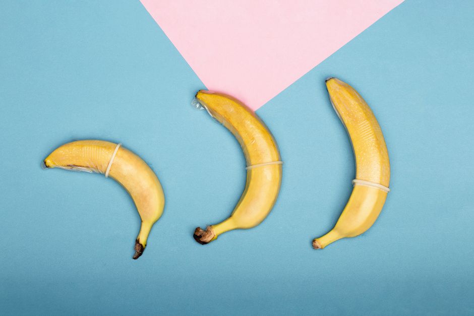 Three bananas wrapped in condoms on a colorful background symbolizing safe sex in a creative way.