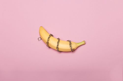 Free A banana wrapped in a metal chain on a pink background, representing conceptual art. Stock Photo