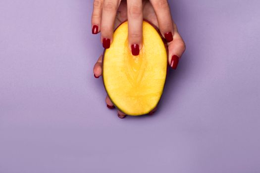 A vibrant image featuring a hand holding a sliced mango on a purple background, showcasing color contrast and texture.