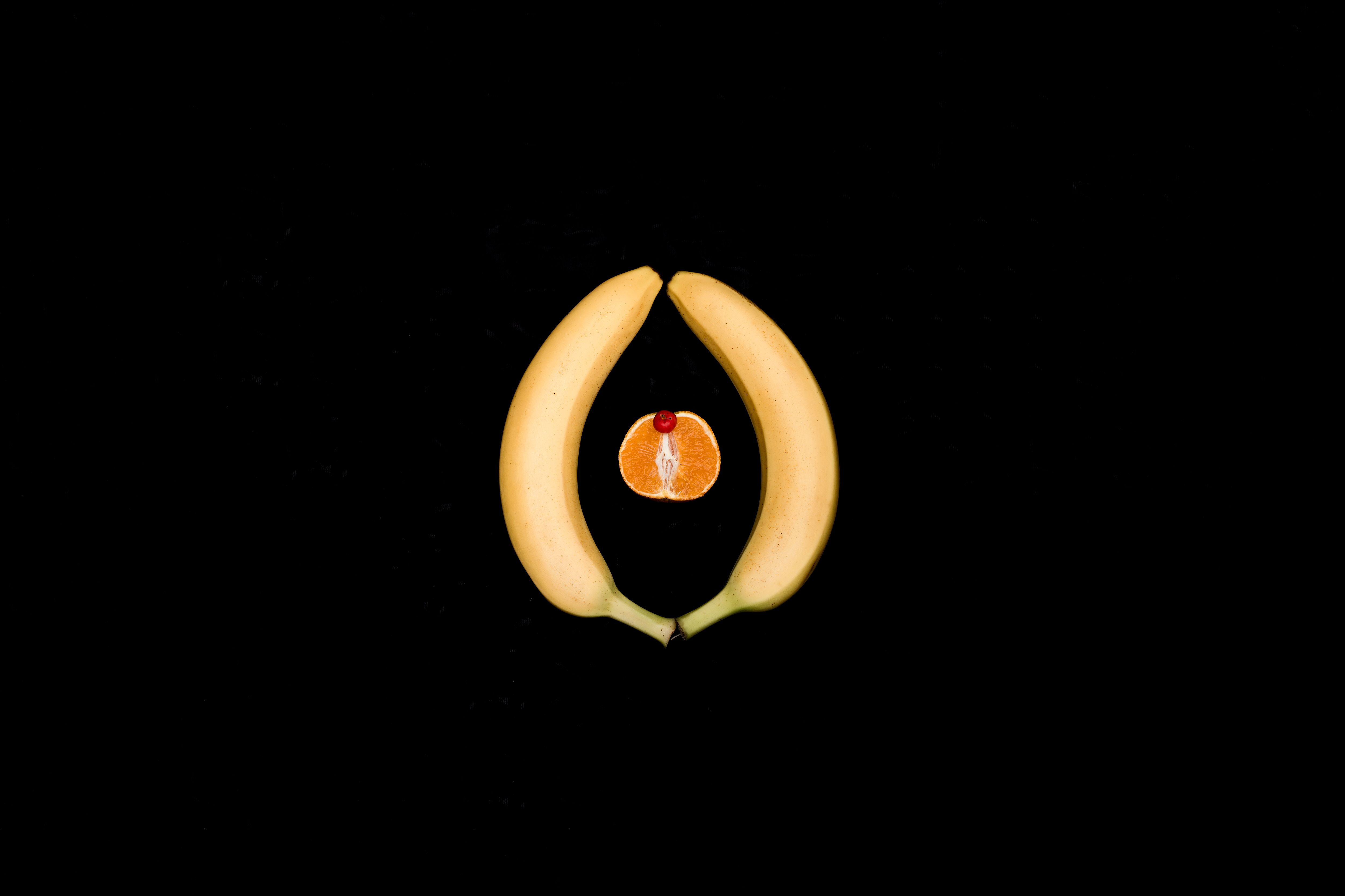 Artistic representation using bananas and orange on black background.