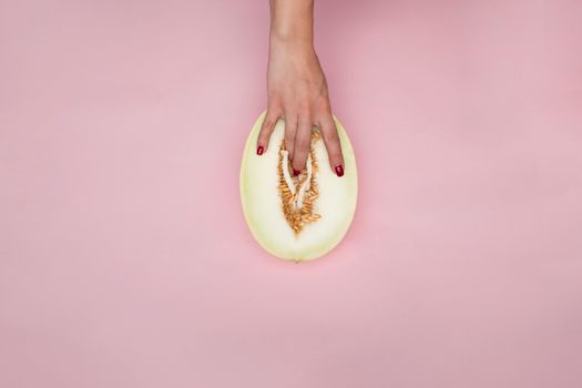 A hand placed on a melon with a pink background, symbolizing abstract concepts.