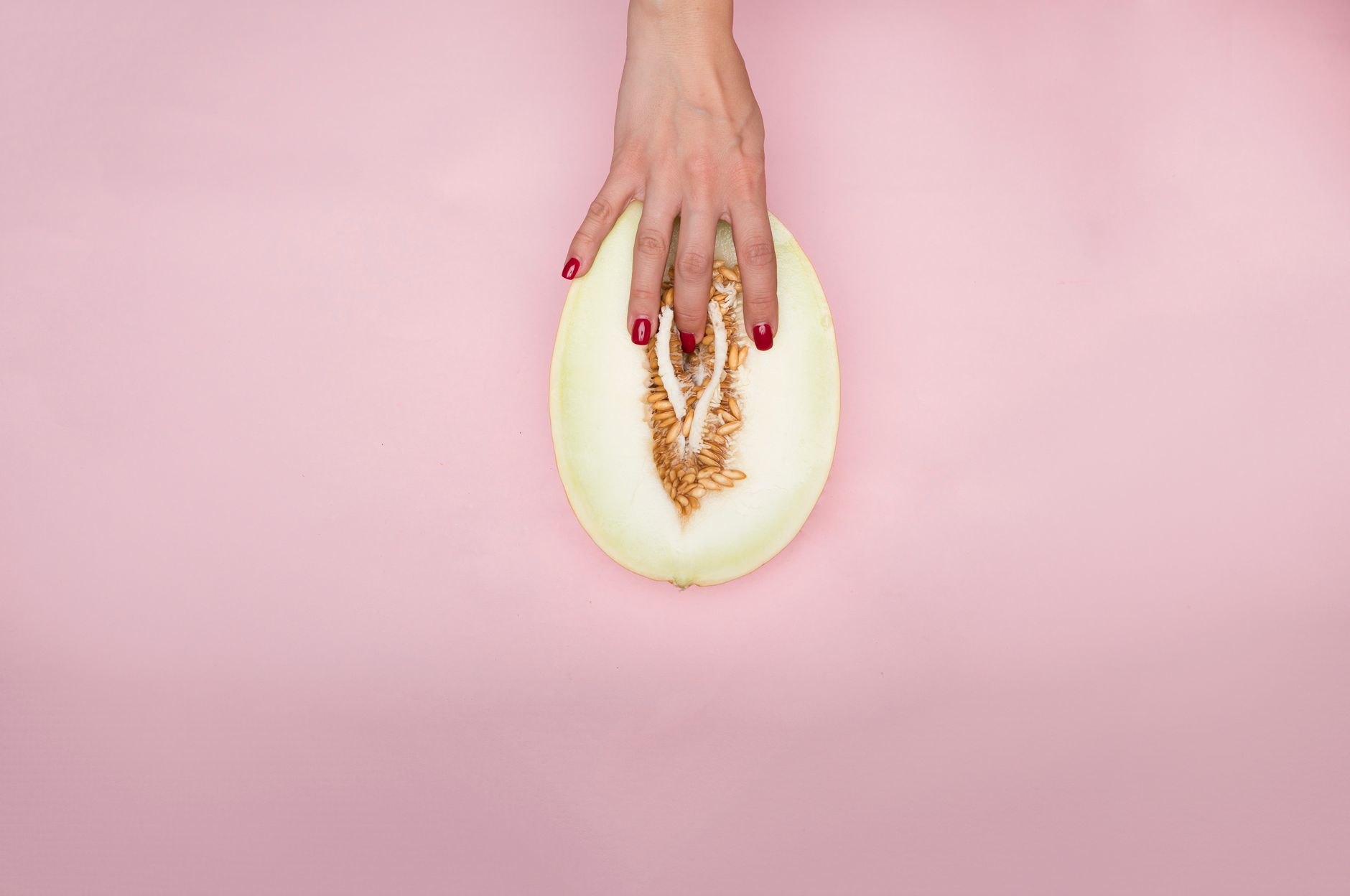 A hand gently touches a melon slice on pink background, emphasizing texture and color.