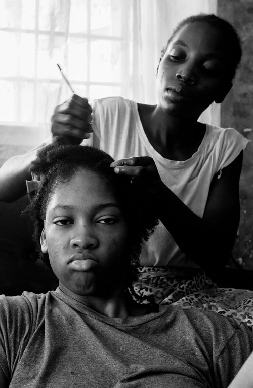 Free Black and white of concentrated African American woman combing hair of dissatisfied teenage  daughter sitting on floor at home Stock Photo