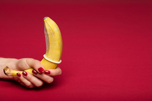 Creative representation of safe sex using a banana with a condom against a red background.