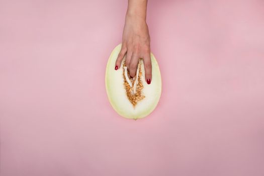 Artistic expression with hand touching a melon, resembling modern conceptual symbolism on a pink backdrop.