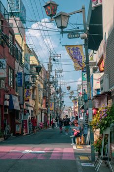 Vibrant urban street scene with shops, lanterns, and pedestrians on a sunny day.