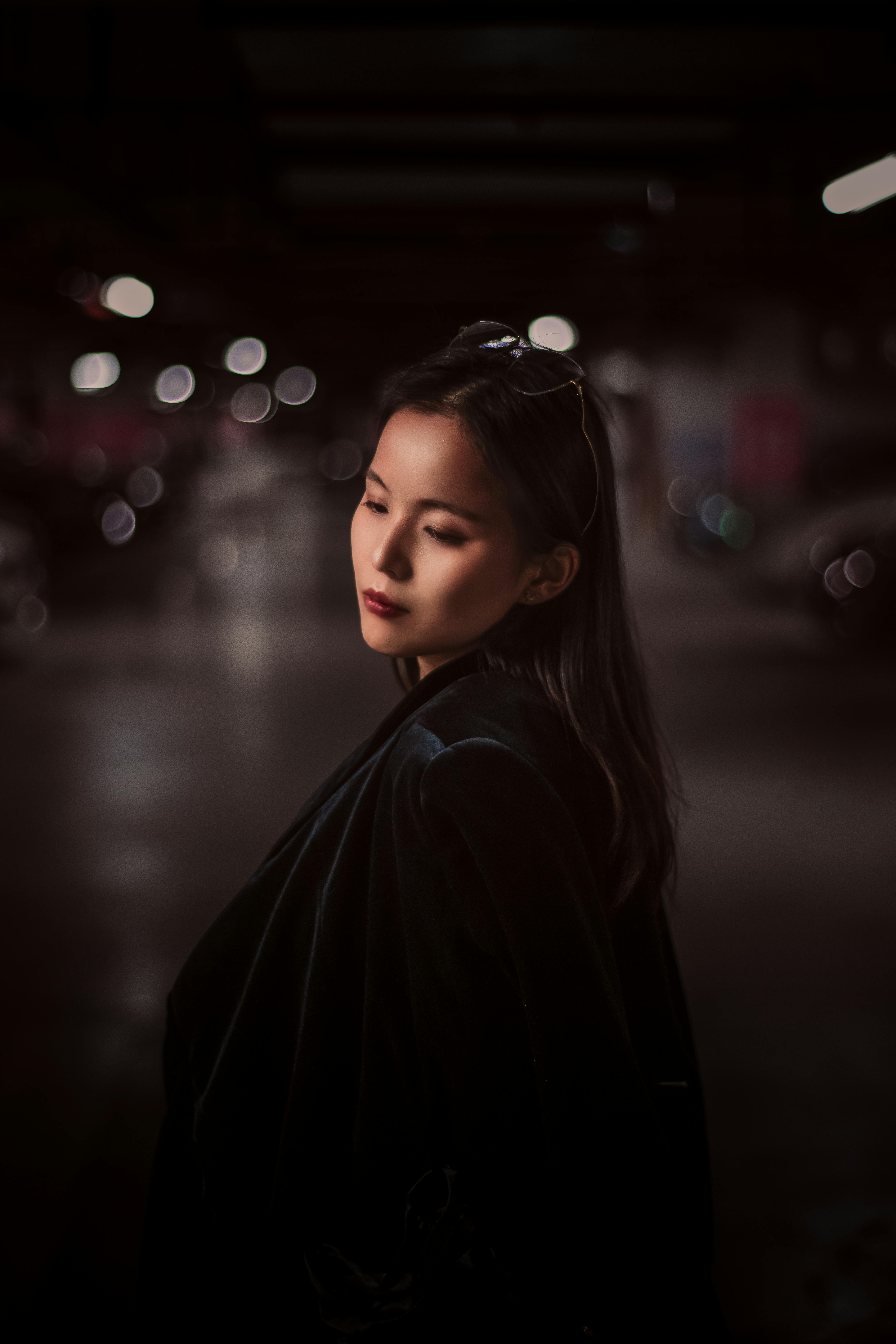 Fashionable young woman in a black jacket posing confidently in a moody nighttime setting.