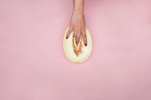 An artistic and conceptual image depicting a hand placed over a melon slice on a pink background.