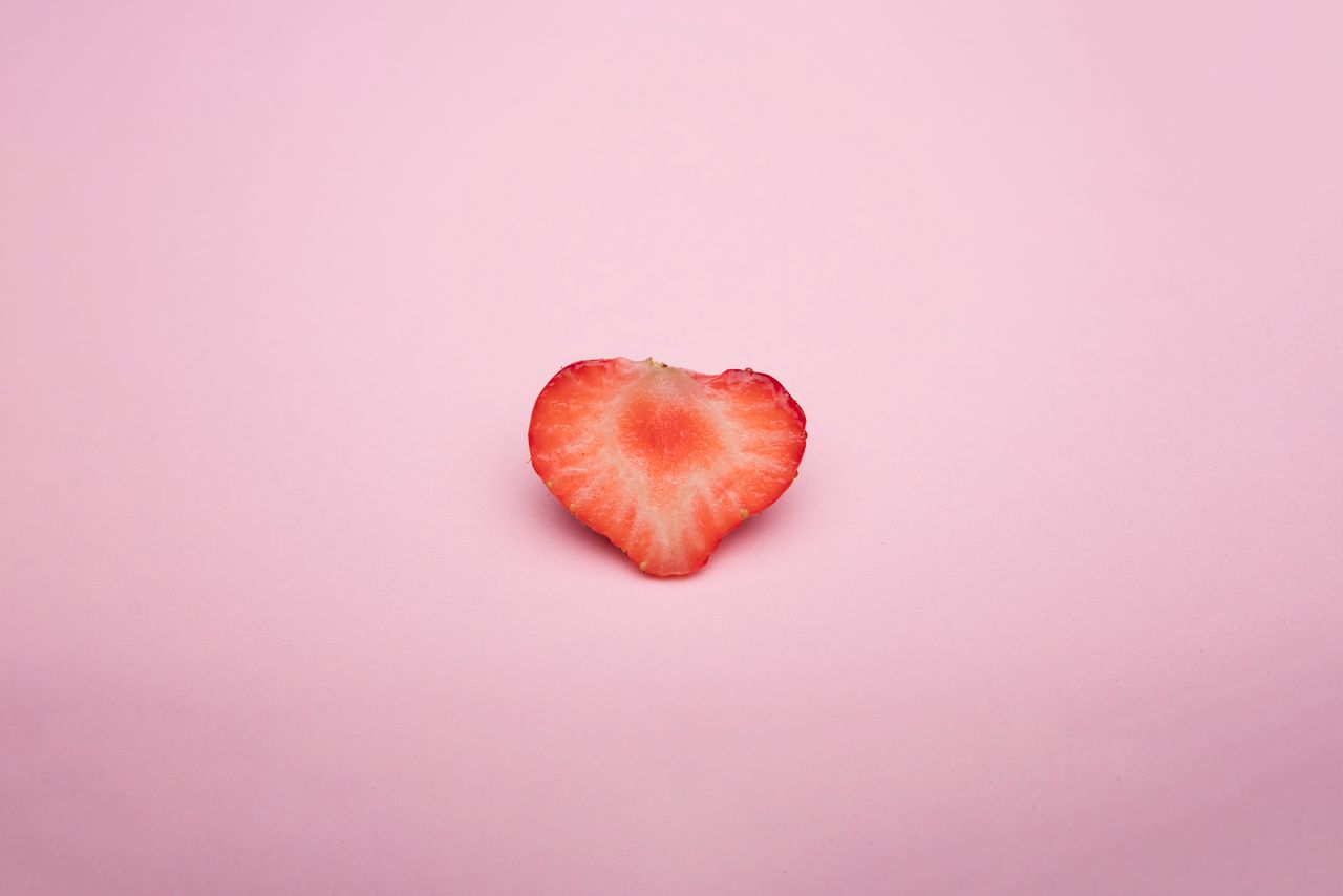 a heart shaped strawberry slice on a soft pink background highlighting
