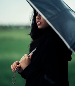 一名年轻的印度妇女撑着伞，在绿地上留下侧面轮廓
