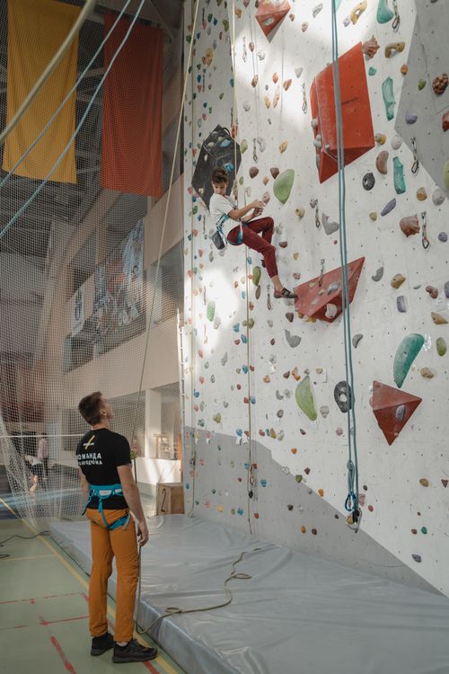 Free A young man practices rock climbing indoors with safety gear and supervision. Stock Photo