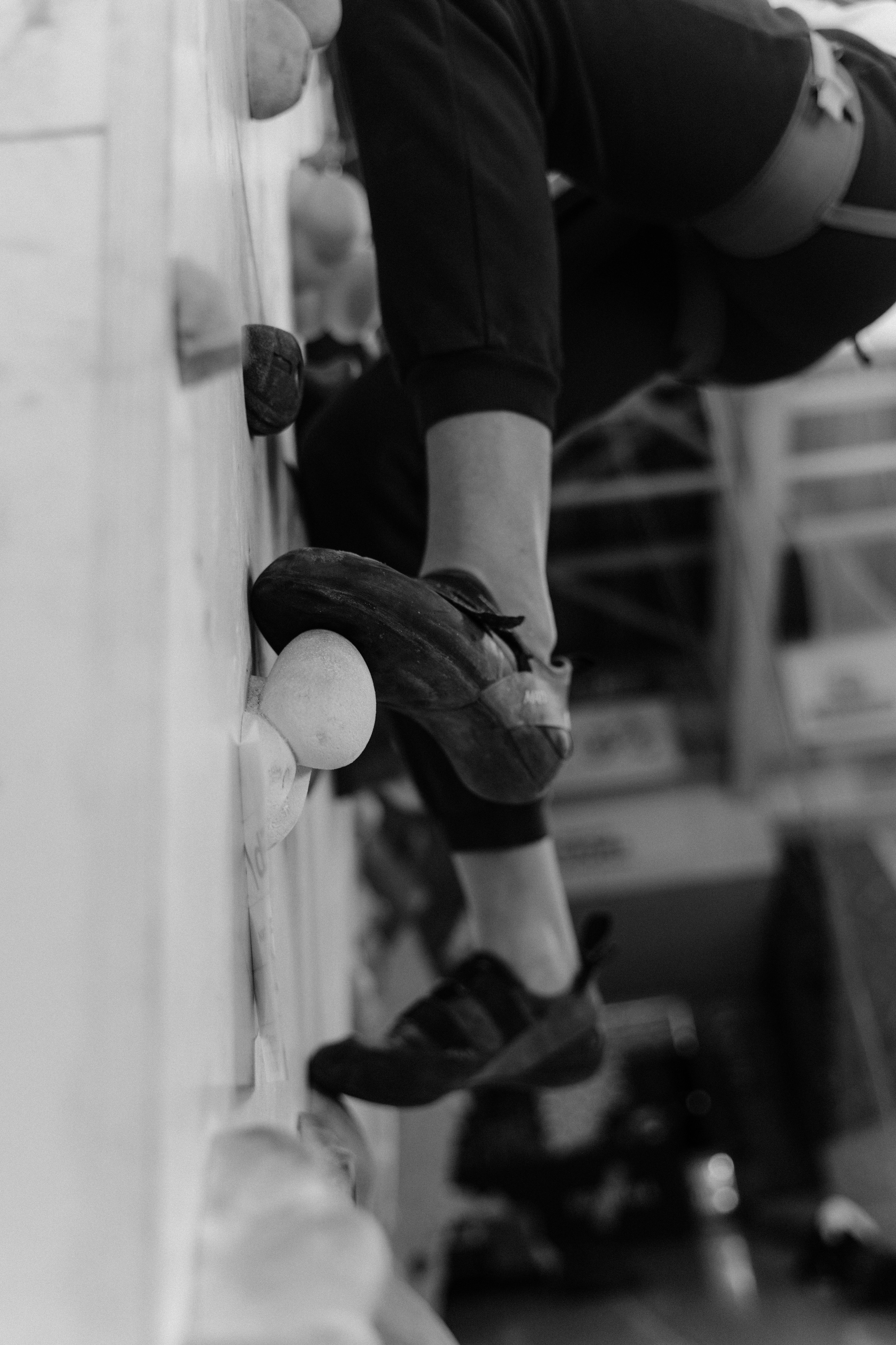 Black and white image of a person climbing an indoor rock wall, focusing on footwork.