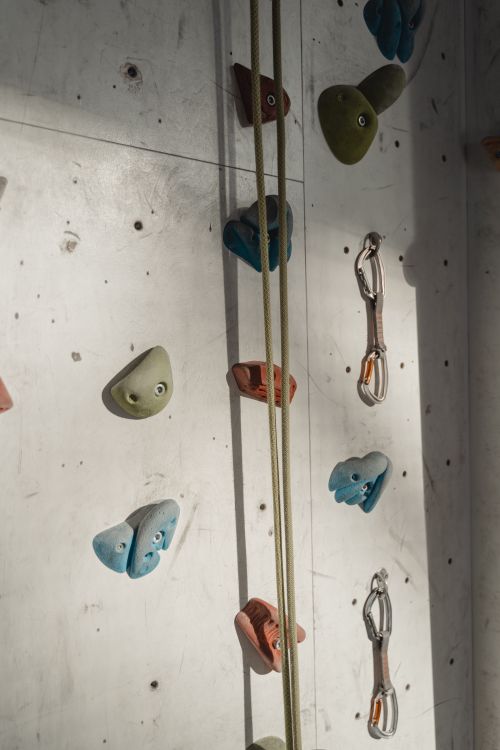 Free Close-up view of an indoor climbing wall featuring colorful holds and carabiners in bright lighting. Stock Photo