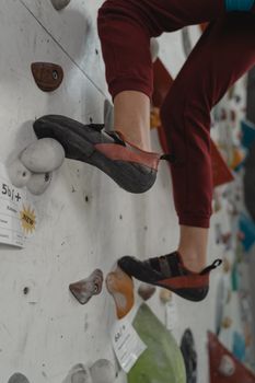 室内墙壁上，一双穿着攀岩鞋的双腿特写，背景是色彩缤纷的握把