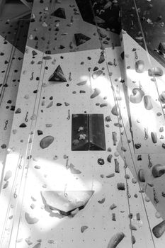 A black and white photo of an indoor rock climbing wall with various grips and ropes.