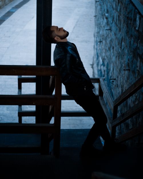 Free A stylish man in a leather jacket leans back on a stair railing, exuding cool confidence. Stock Photo