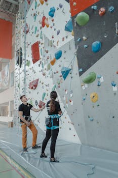 Two adults engaging in an indoor rock climbing activity with focus on teamwork and fitness.